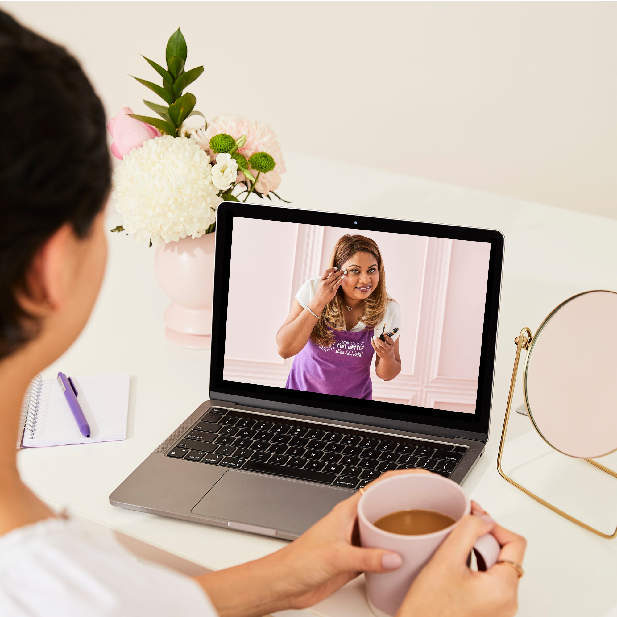 Woman watching an online Look Good Feel Better workshop on a laptop while holding a cup of coffee.