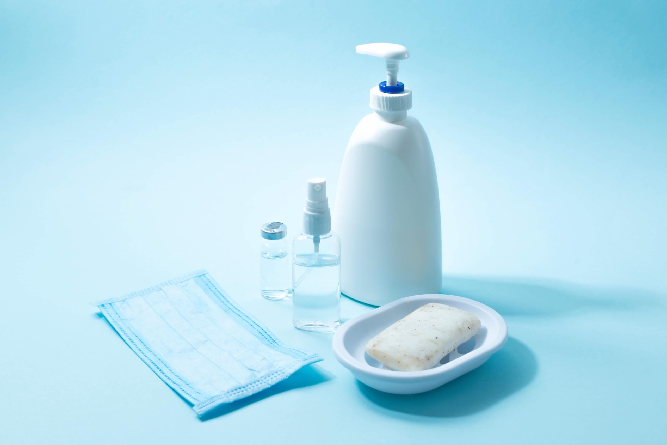 Hand sanitizer, soap, face masks, and disinfectant spray on a blue background.