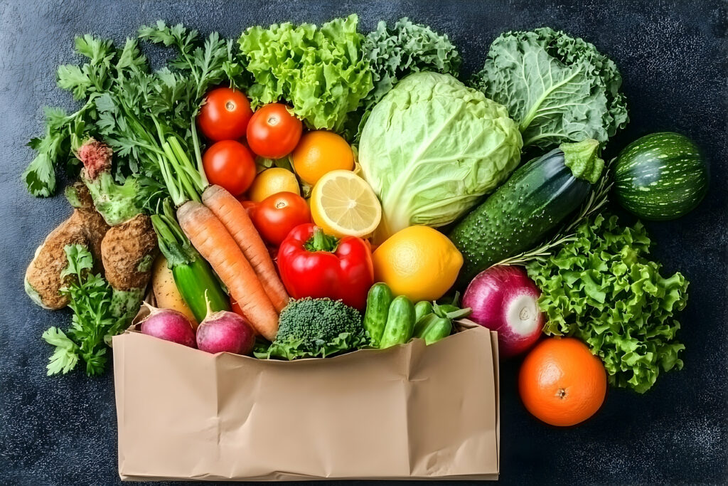 Fresh vegetables and fruits spilling from a paper bag, including lettuce, carrots, tomatoes, cabbage, cucumbers, citrus, and peppers.