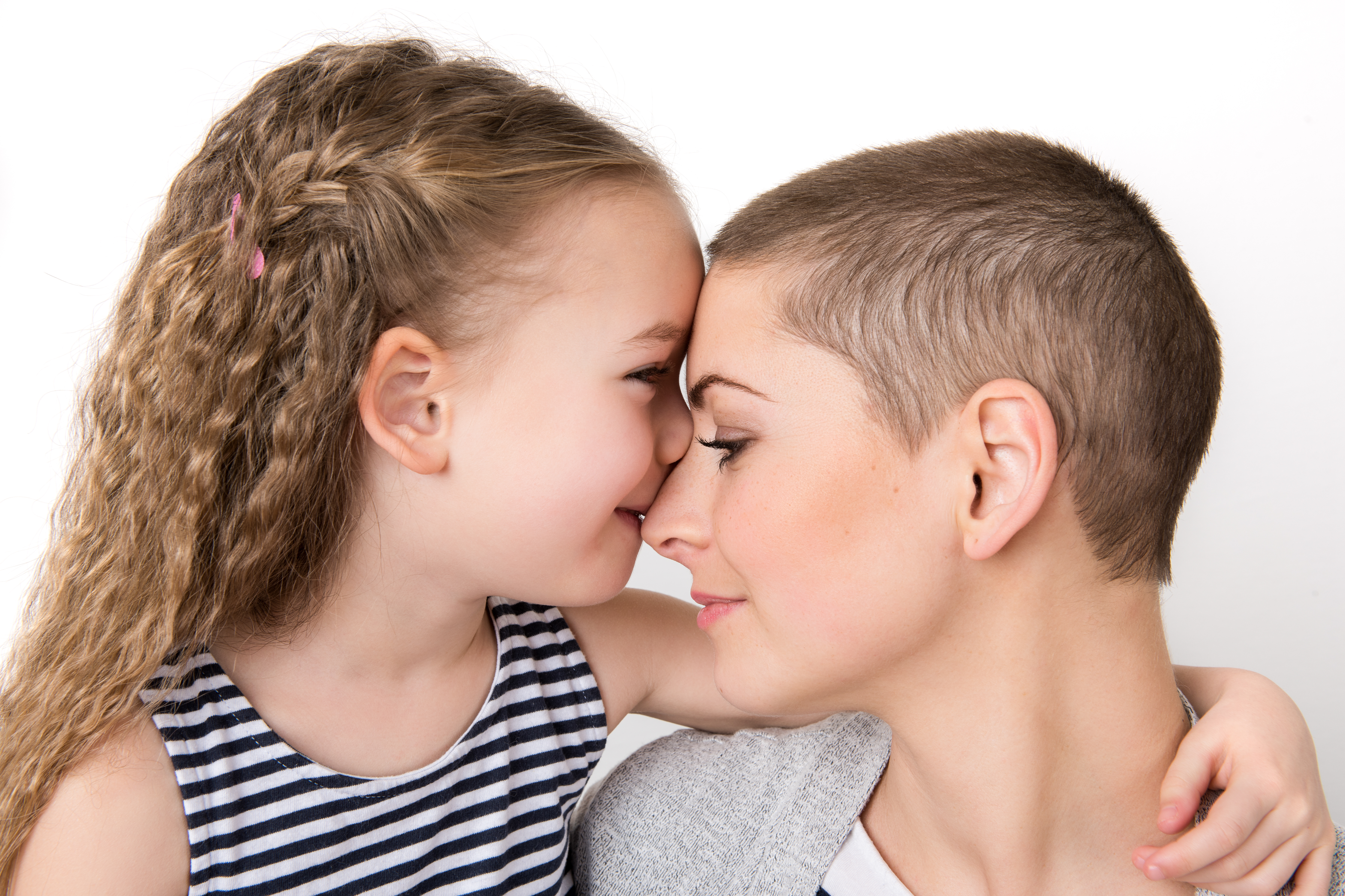 A preschool aged girl nuzzled up to her mother who has a buzzcut.