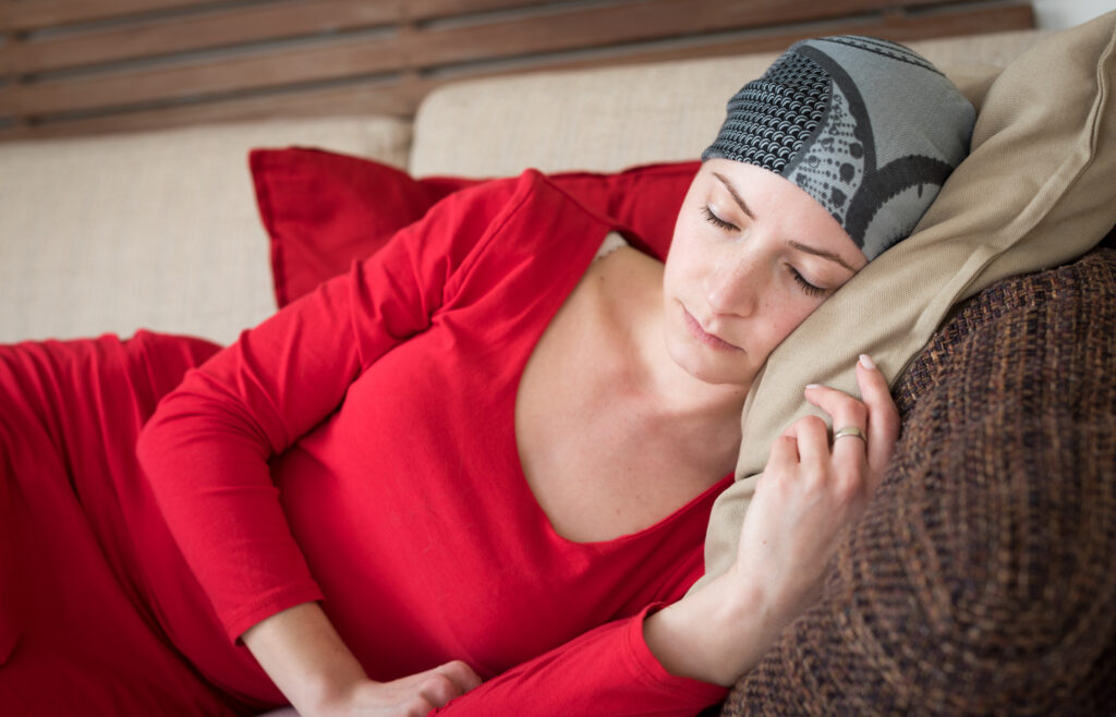 A young female cancer patient resting on a couch with her eyes closed.