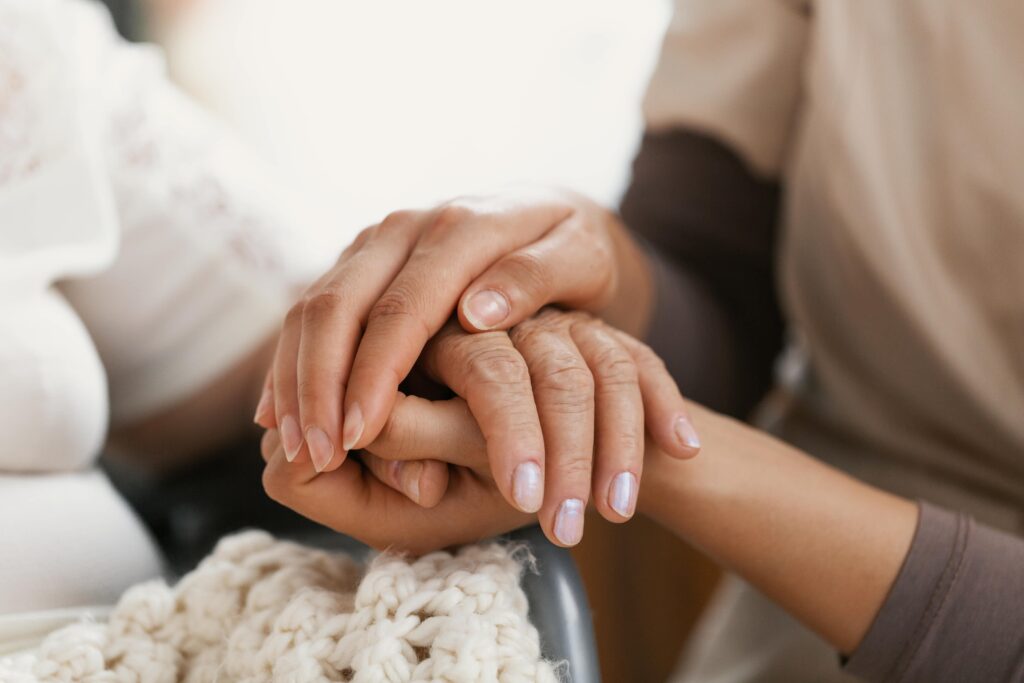 Close‑up of a young woman’s hand gently holding the hand of an older lady.