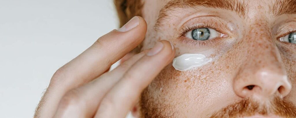 A close-up of a man applying thick eye cream under his eye.