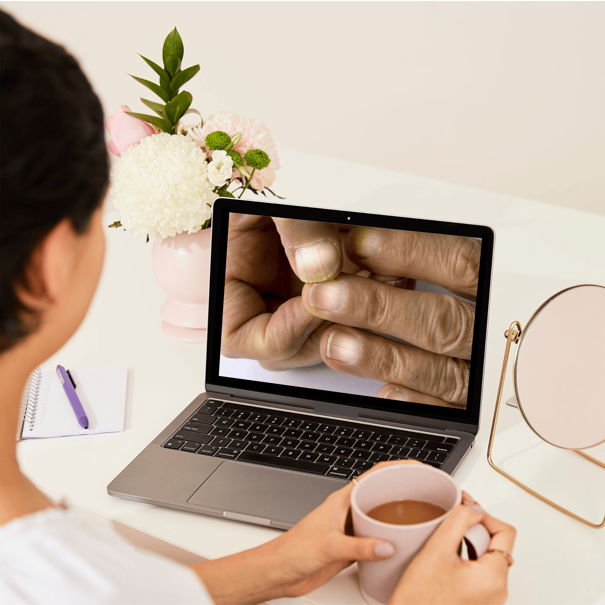 Over-the-shoulder view of a woman at a desk looking at a nail care workshop on a laptop.