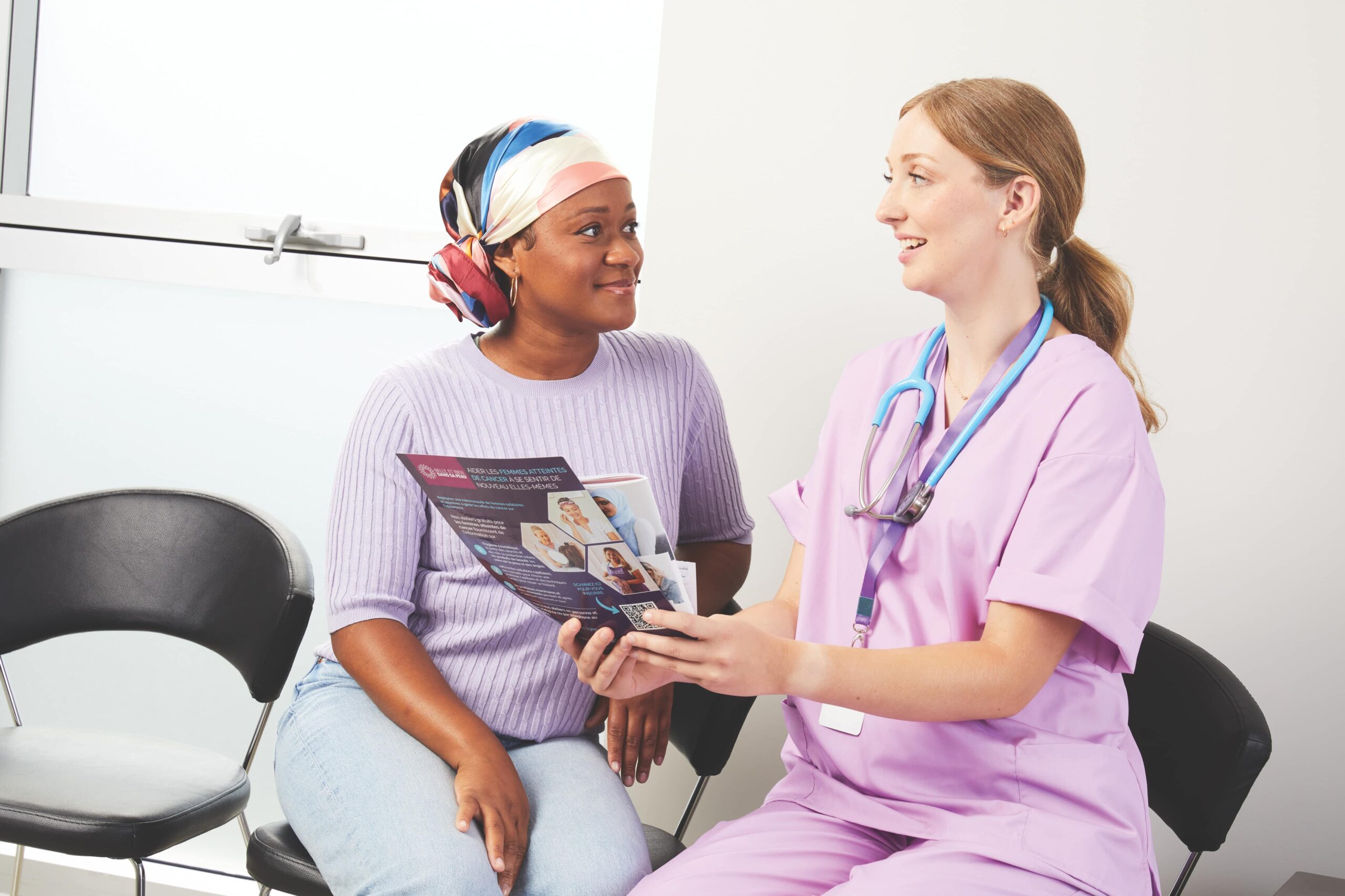 Une infirmière en blouse violette montre une brochure à un patient atteint d'un cancer, tous deux souriants.