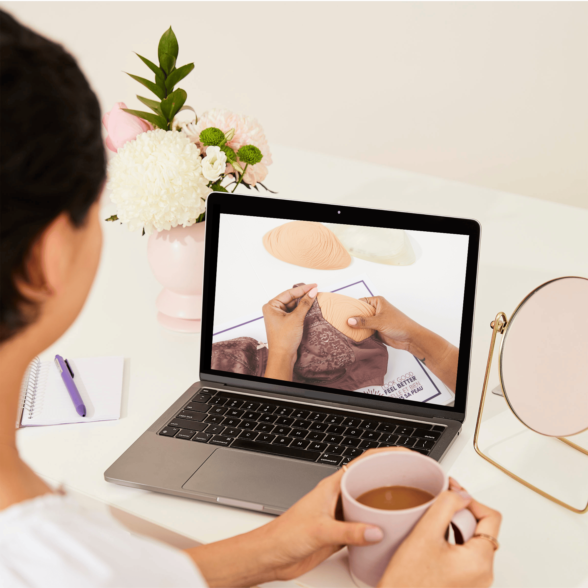 Over-the-shoulder view of a woman at a desk looking at bras and prostheses images on a laptop.