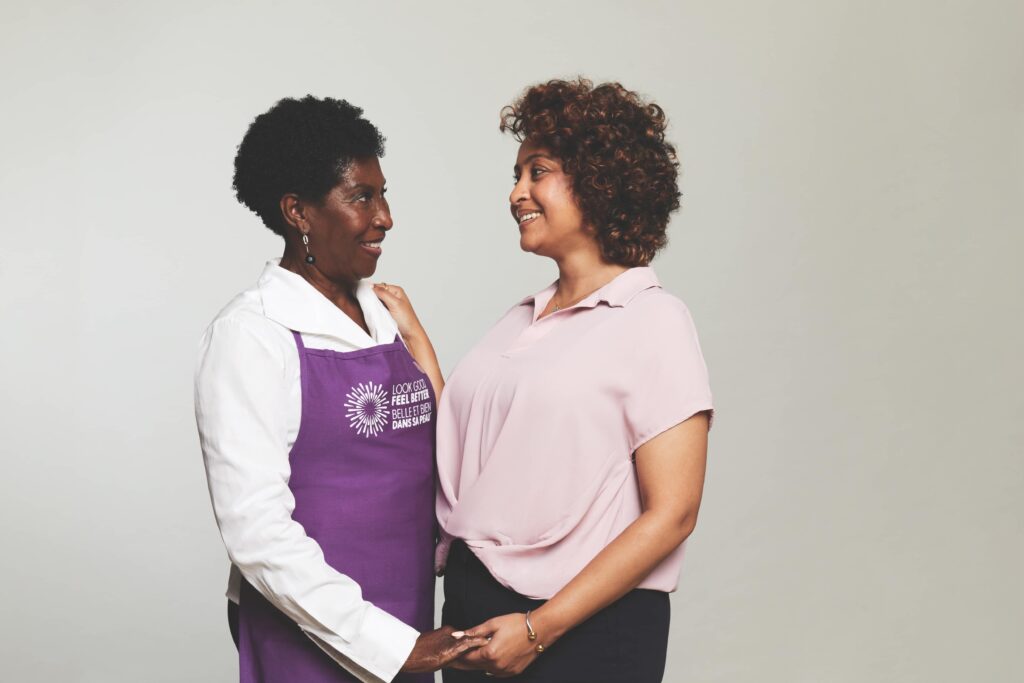 A Look Good Feel Better volunteer and a participant smile at each other while holding hands.
