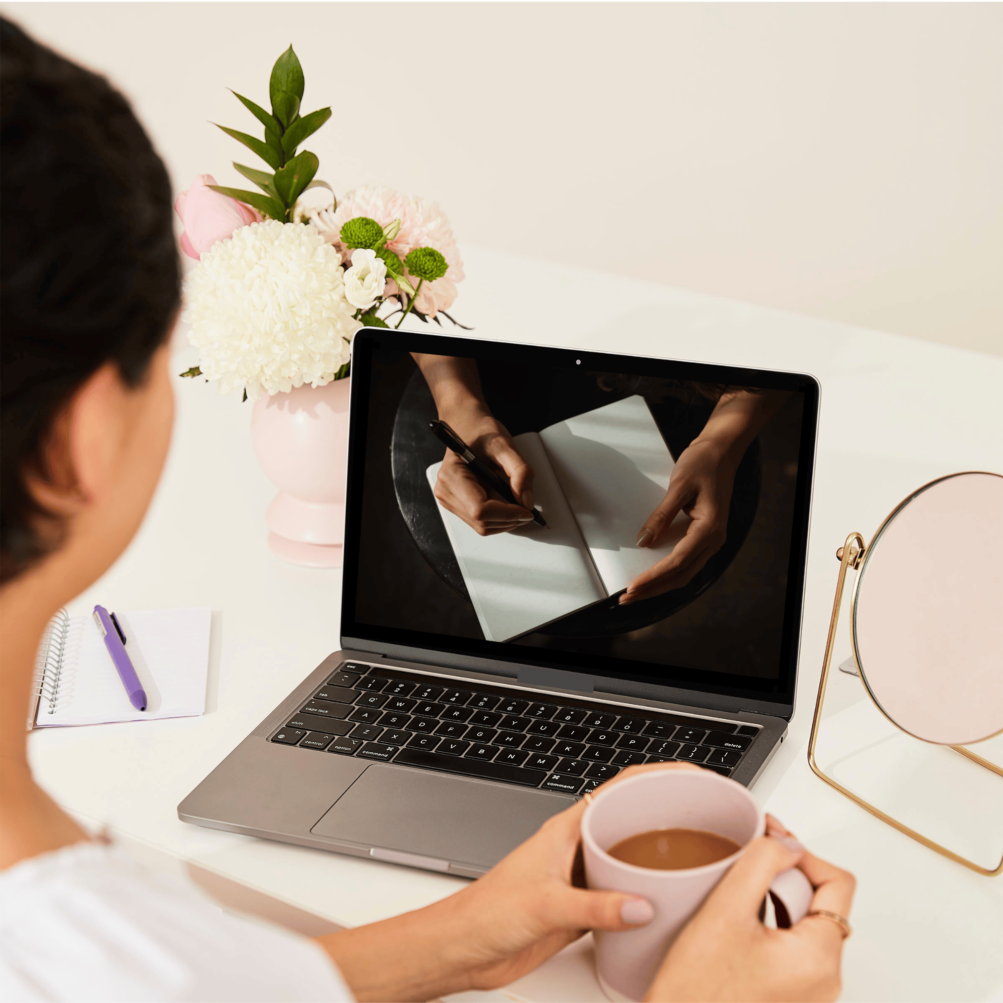 Over-the-shoulder view of a woman at a desk looking at a workshop on a laptop.