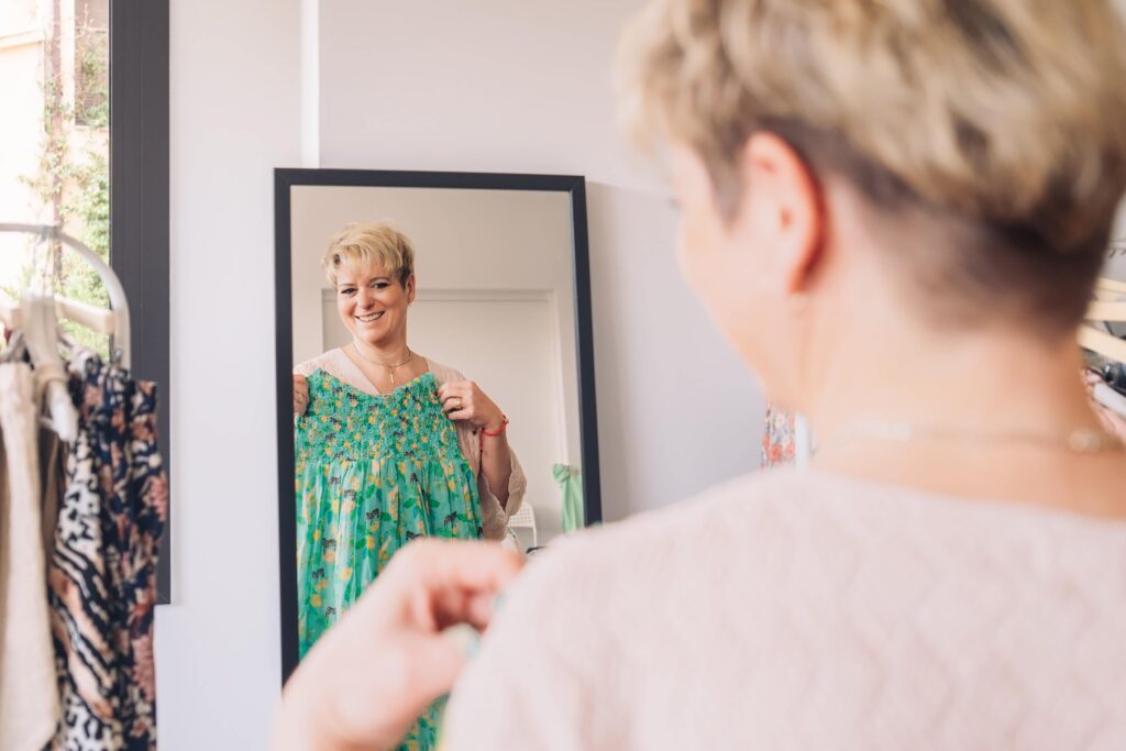 A woman looking into a mirror holding up a dress to her chest.